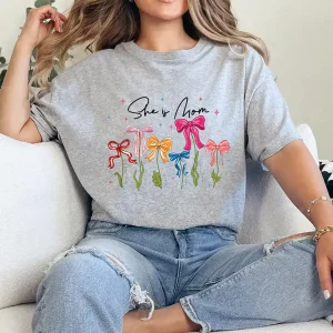 She Is Mom T-Shirt – Retro Coquette Bow Christian Mom Shirt, Bible Verse 'She Is Strong' Tee, Cute Mother's Day Gift for Faithful Mama