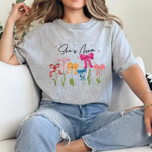 She Is Mom T-Shirt – Retro Coquette Bow Christian Mom Shirt, Bible Verse 'She Is Strong' Tee, Cute Mother's Day Gift for Faithful Mama